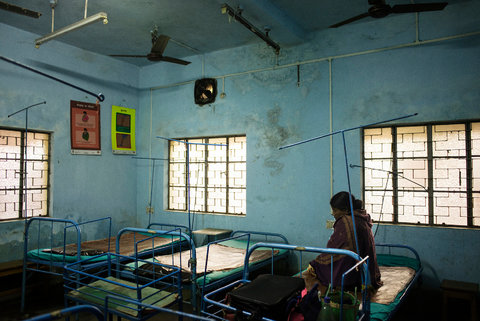 Basic hospital ward in South Asia with metal beds, ceiling fans, and limited medical equipment.